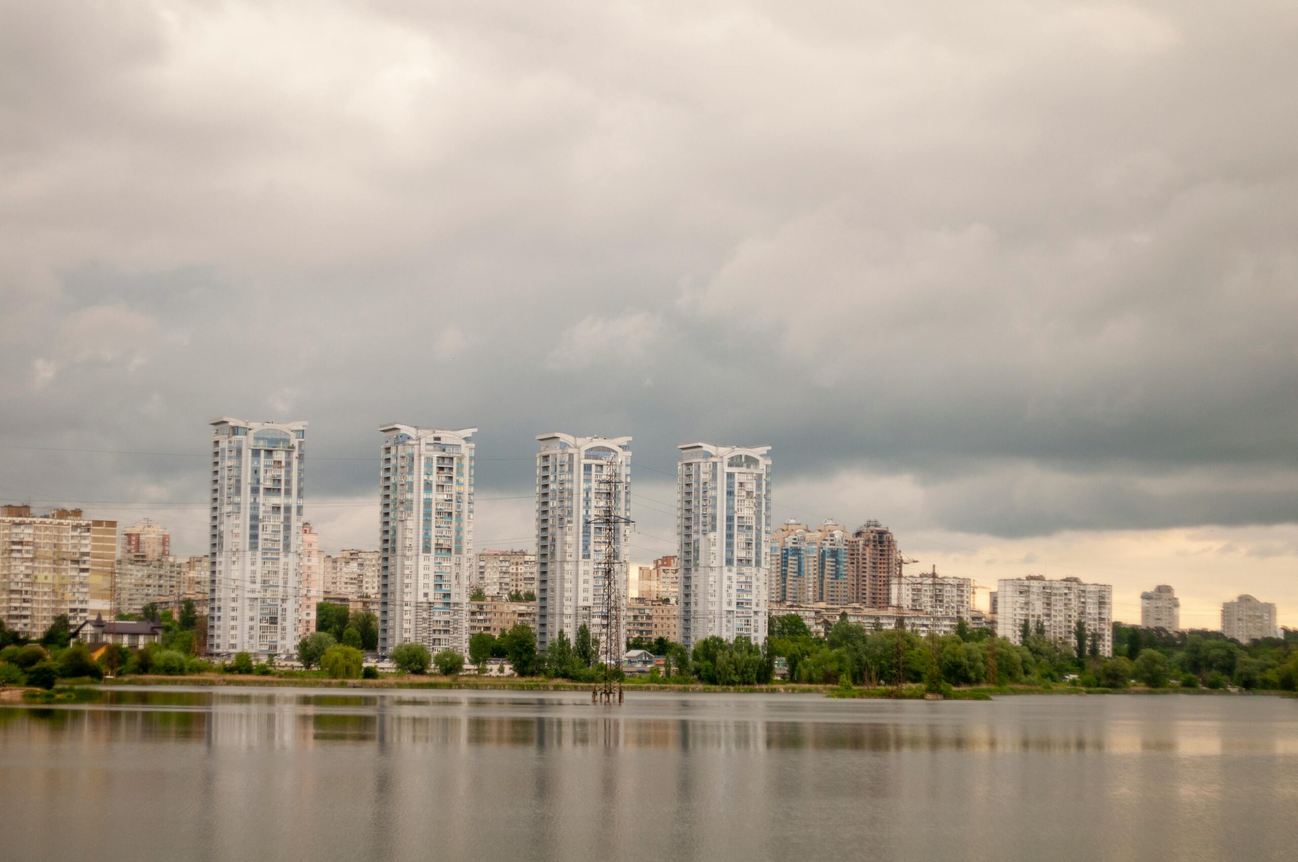 Skyscrapers along a tranquil river under a cloudy sky in an urban landscape.